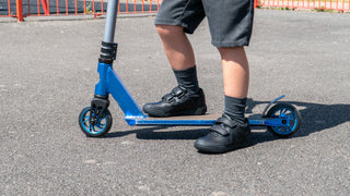 Boy wearing black touch fasten school trainers on a blue scooter