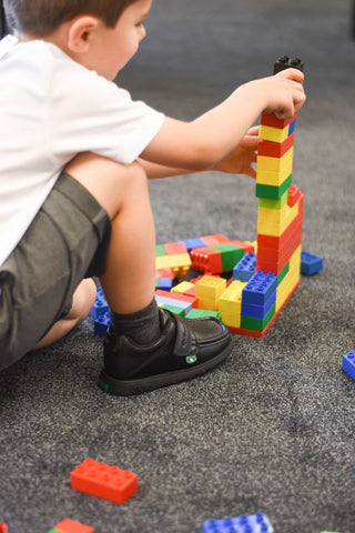 boy playing on a carpet with building blocks in kicker school trainers